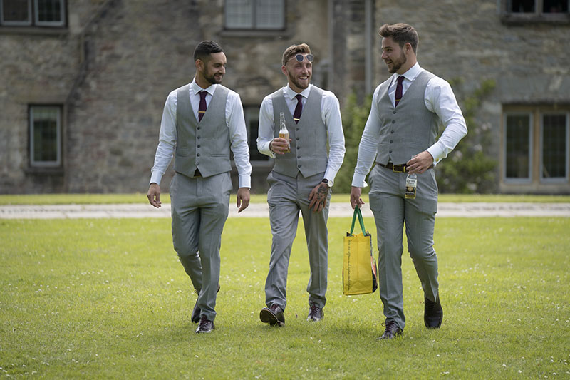 3 Groomsmen walking along the lawn at Dartington Hall